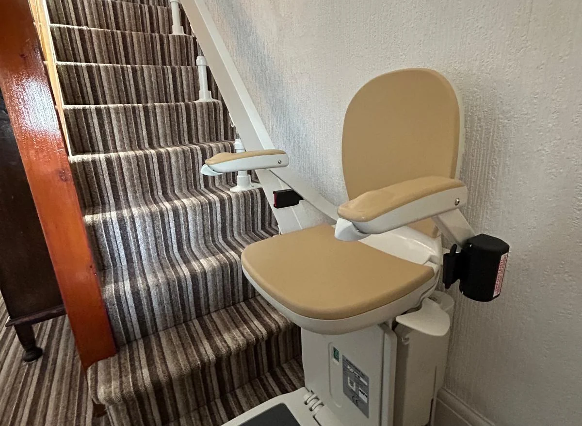 Stairlift seat and straight rail fitted beside a striped patterned stair carpet